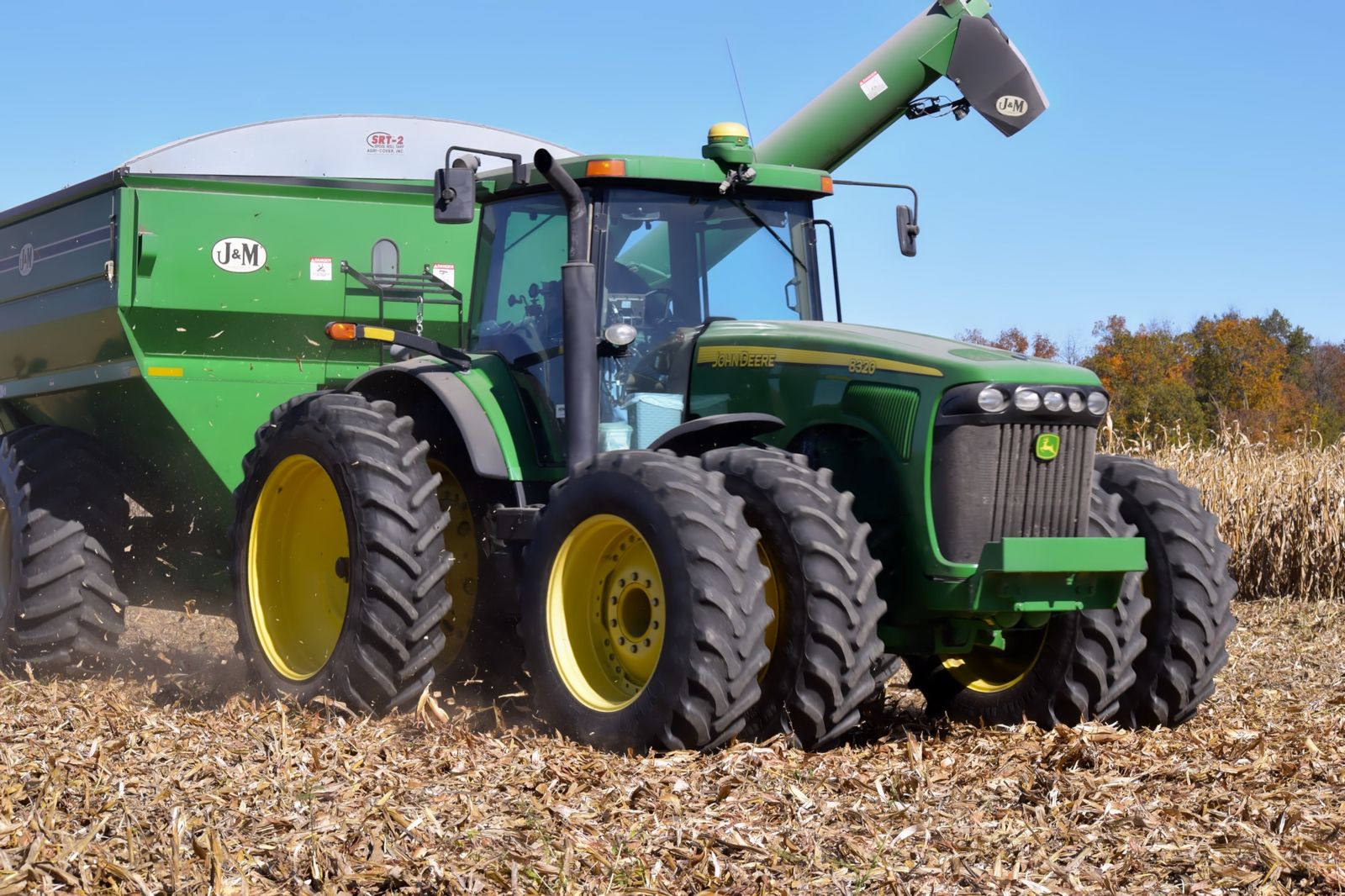 John Deere tractor pulling a J&M grain cart through a harvested corn field