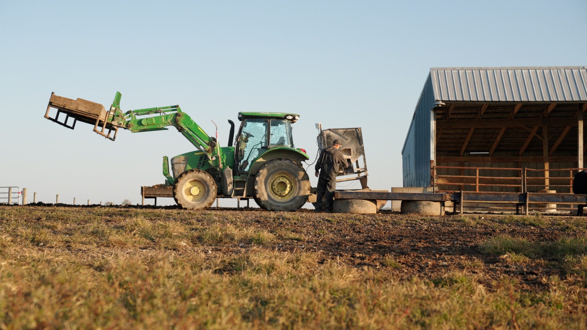 Farmer working beside a John Deere utility tractor with front loader on a Koenig customer farm