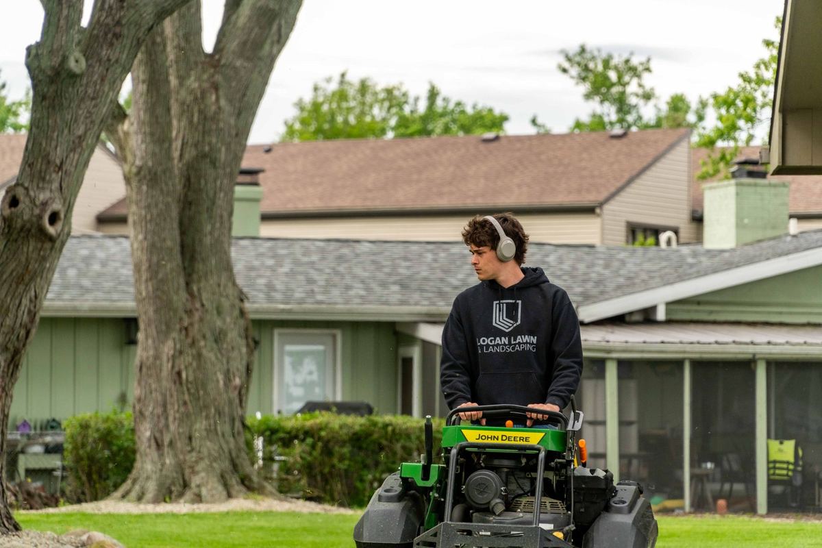 Logan Lawn & Landscaping crew member on a John Deere QuikTrak stand-on mower