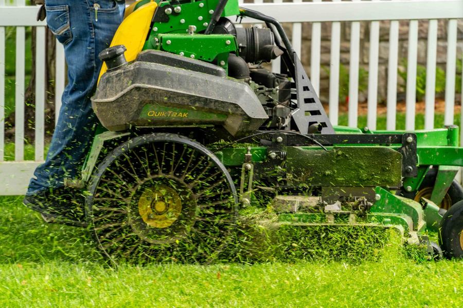 John Deere QuikTrak stand-on mower cutting grass along a fence line