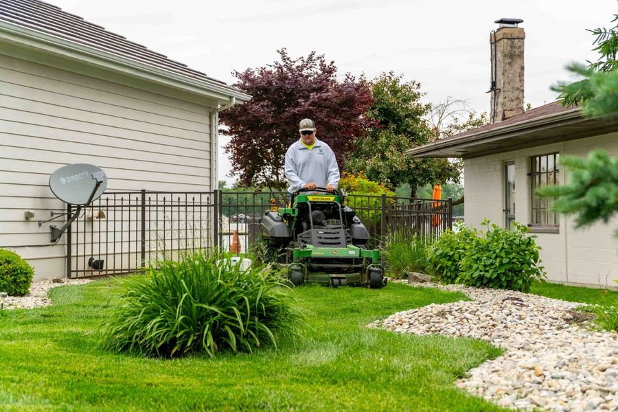John Deere stand-on mower working around landscaped beds