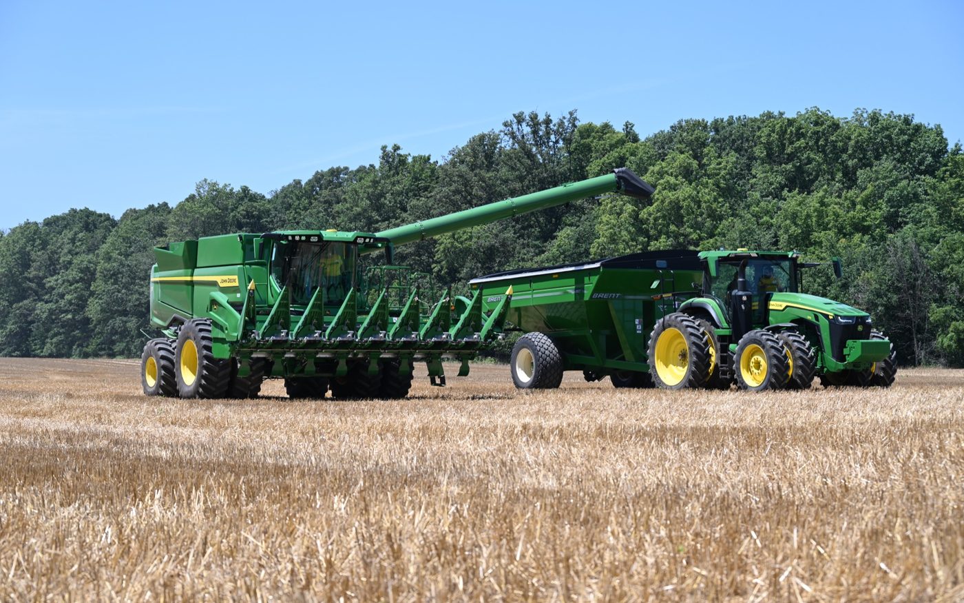 A John Deere S780 combine beside an 8R tractor and grain cart at harvest
