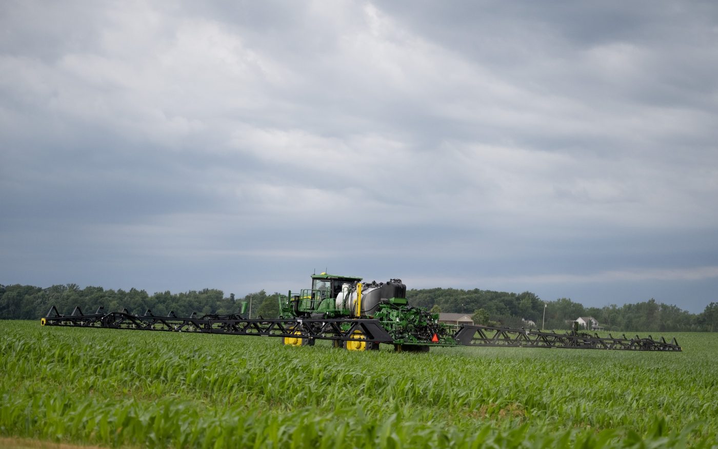 A John Deere self-propelled sprayer applying product across a field of young corn