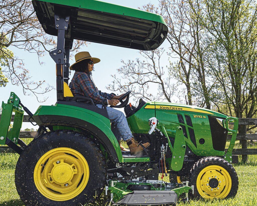 Woman driving a green and yellow John Deere 2032R tractor with a canopy in a grassy field