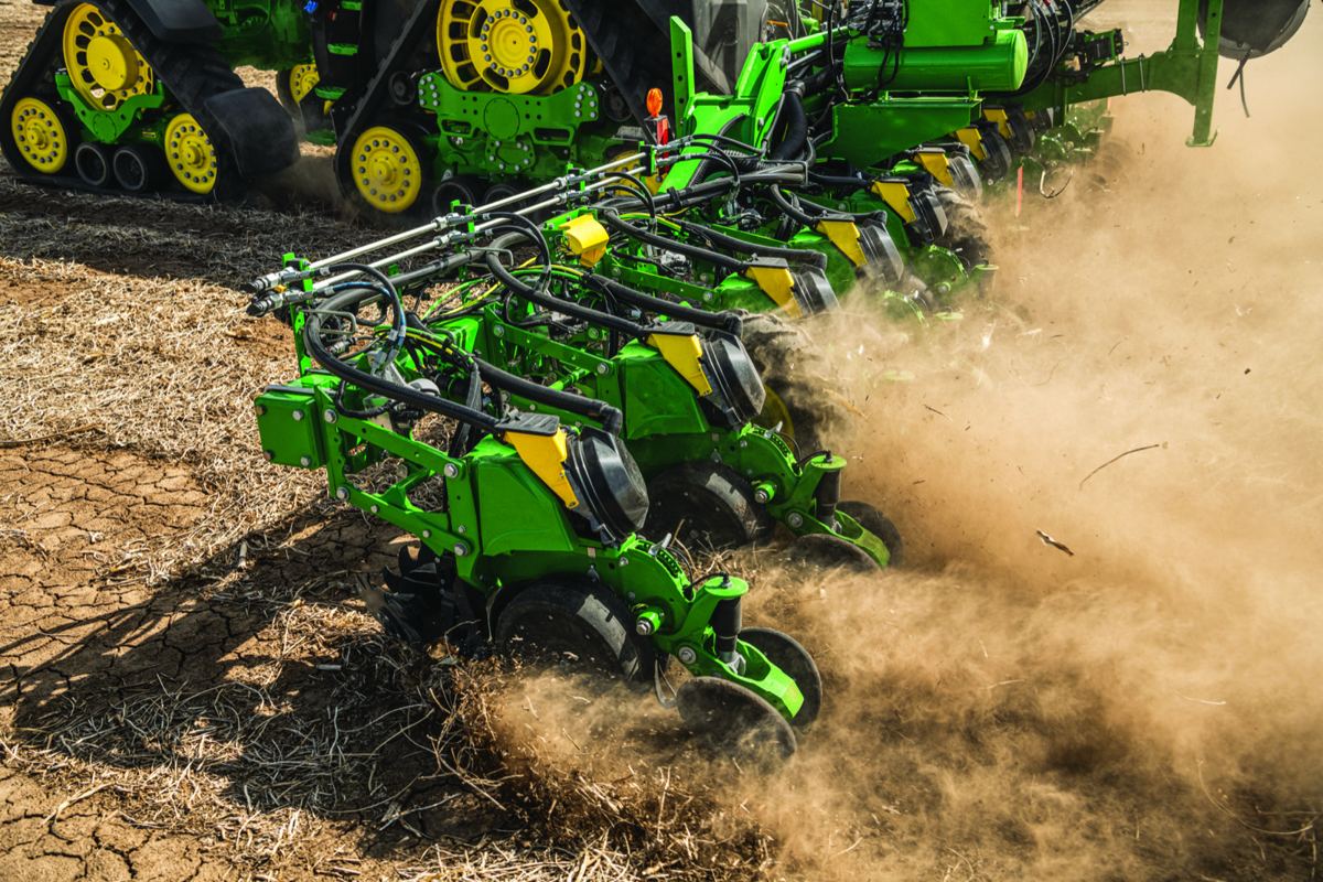 Green and yellow John Deere farm equipment, a tracked tractor and a multi-row planter, working in a dry, dusty field
