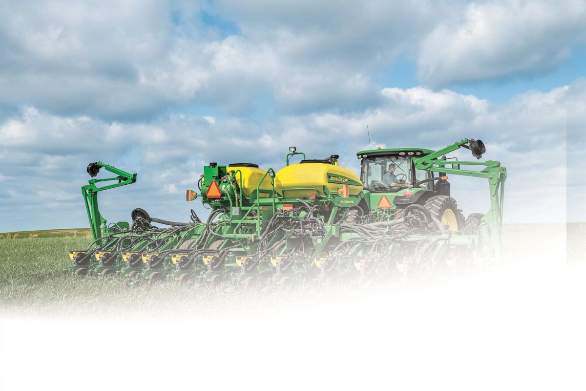 Man driving a John Deere tractor pulling a large green planter with yellow tanks in a crop field