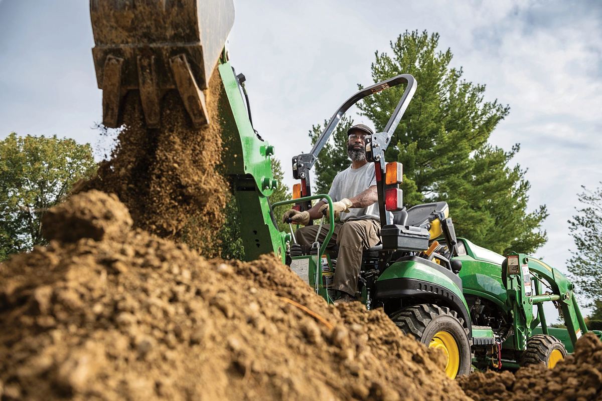 Man operating a green John Deere tractor with a front-end loader dumping dirt
