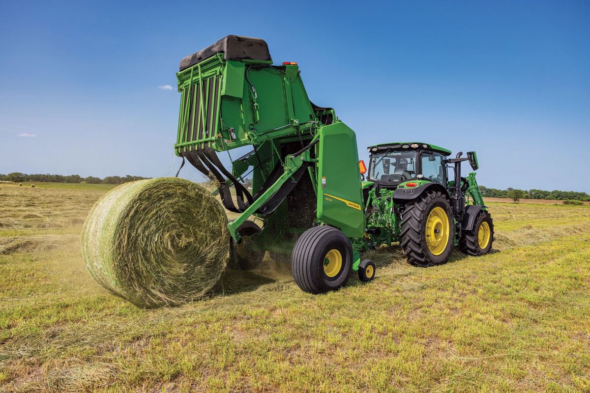 John Deere tractor pulling a 460R round baler ejecting a large hay bale in a field