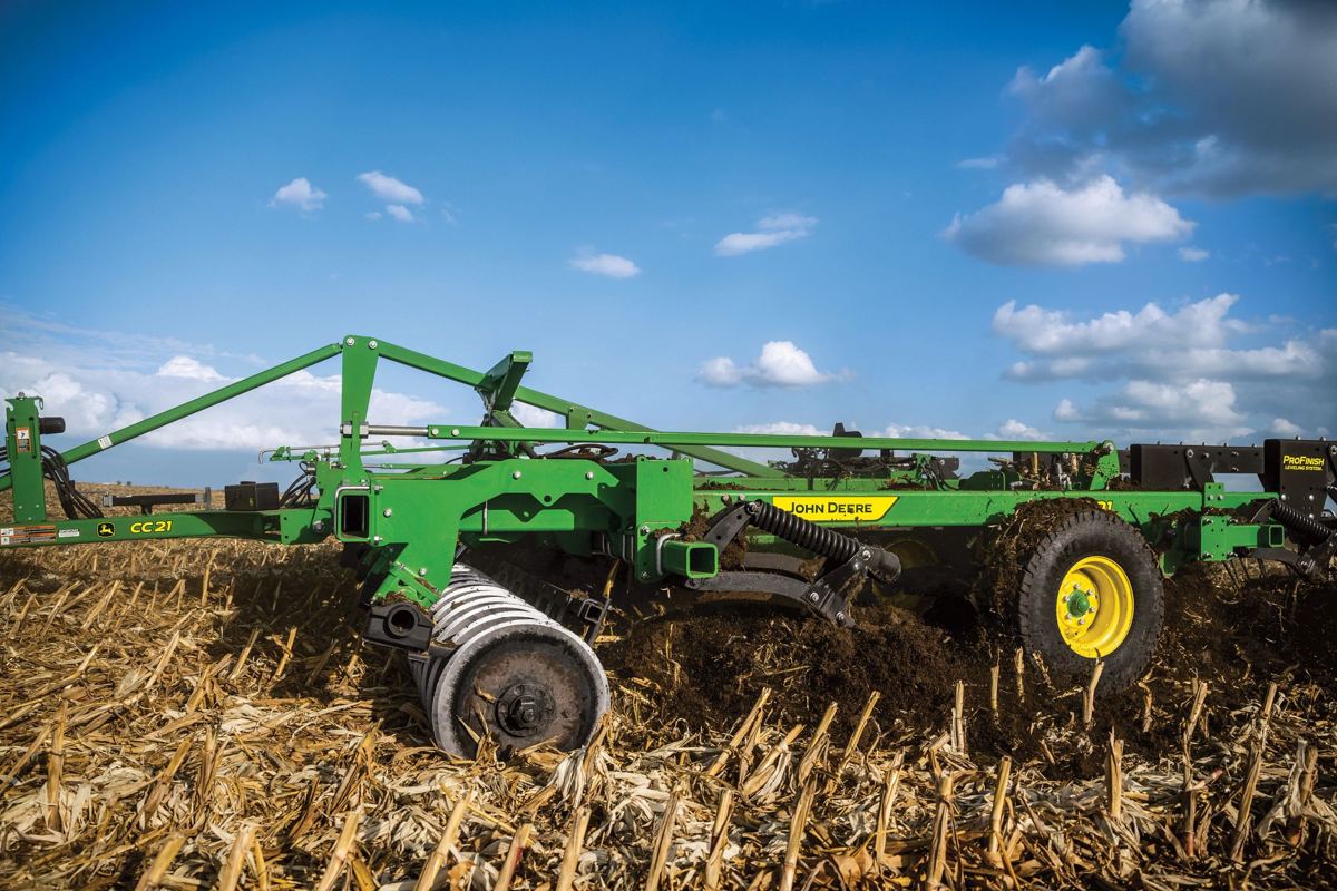 John Deere CC 21 farm implement tilling a field of harvested corn stalks under a cloudy sky