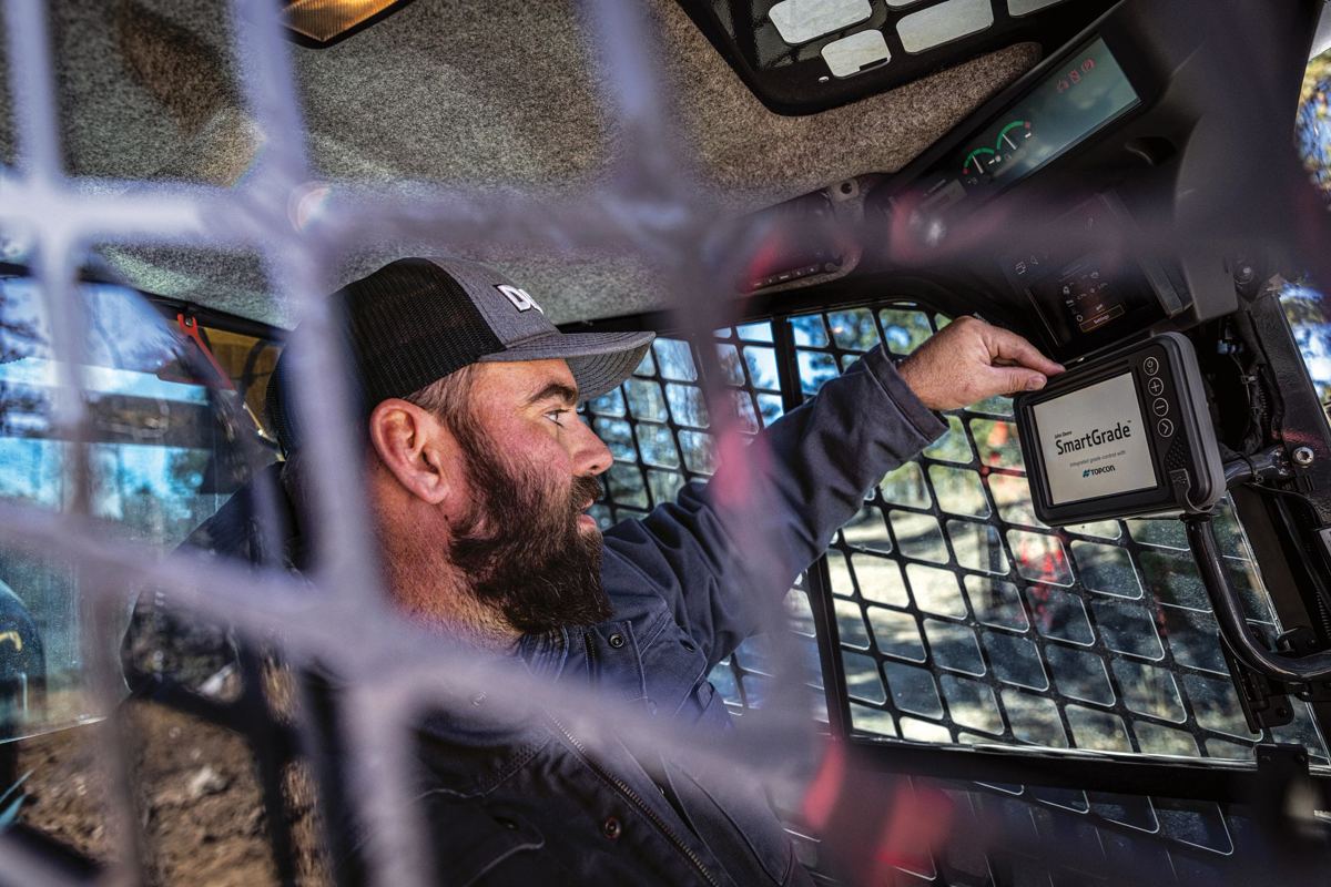 A man is shown operating a John Deere compact track loader from inside the cab, interacting with the controls on a jobsite