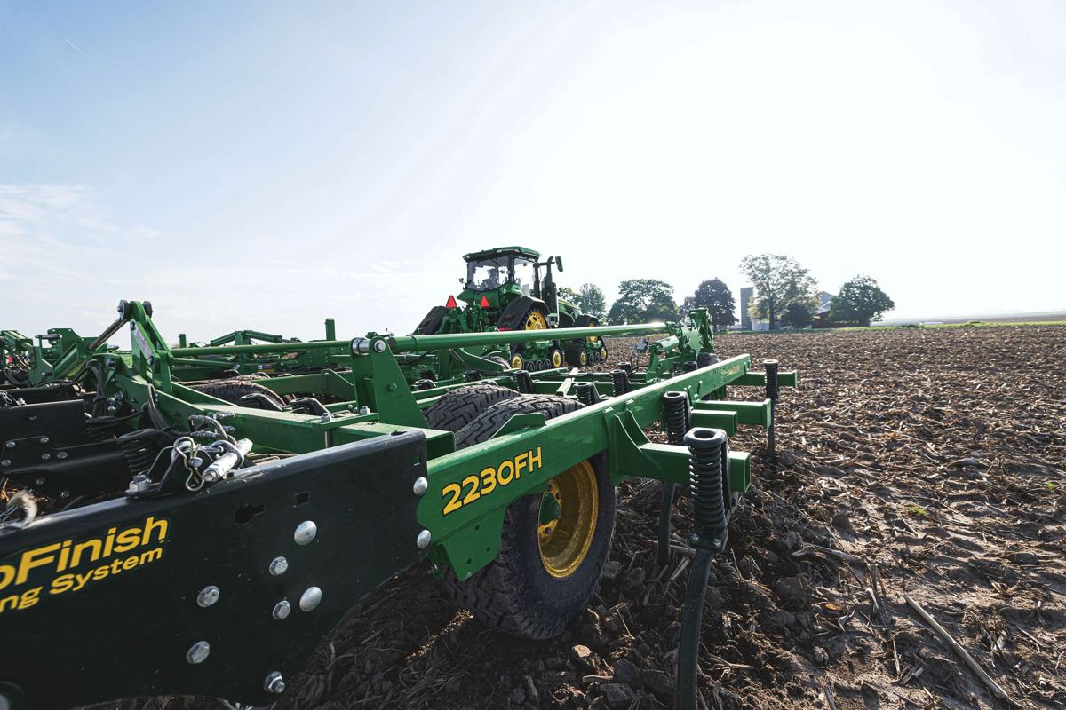 John Deere 2230FH tillage equipment in a field with a John Deere tractor and farm buildings in the background