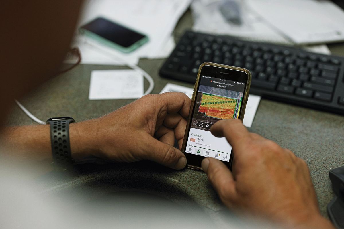 Person's hands holding a smartphone showing a 2023 wheat harvest yield map with colored data