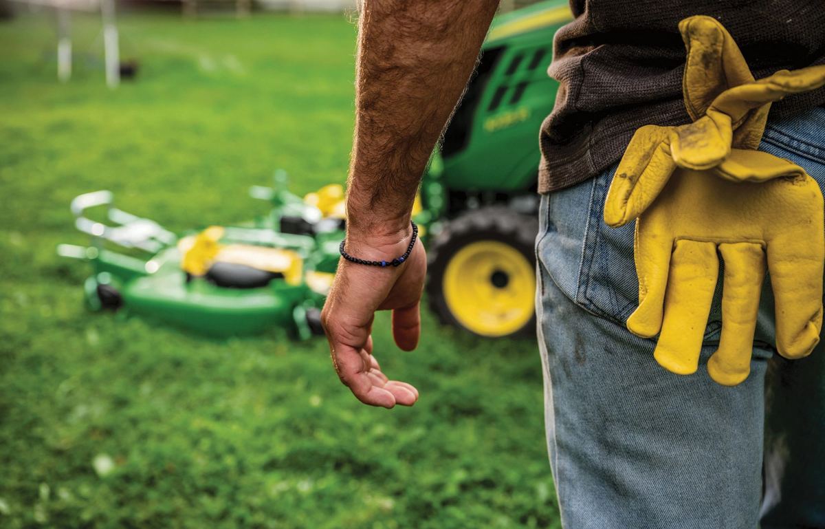 Close-up of a person's arm and side with a work glove in jeans pocket, near a John Deere mower