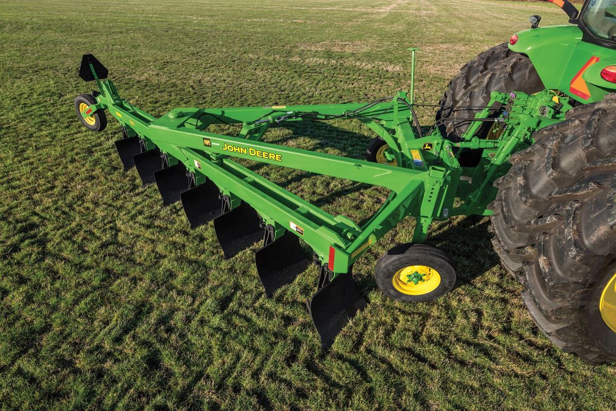 Green John Deere plow attached to a John Deere tractor in a grassy field