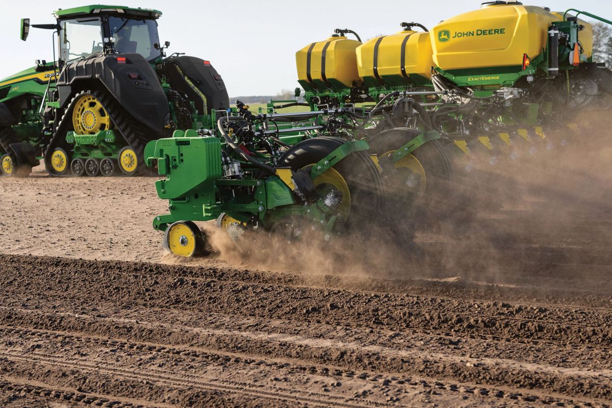 John Deere tracked tractor pulling a multi-row ExactEmerge planter working in a field, kicking up dust