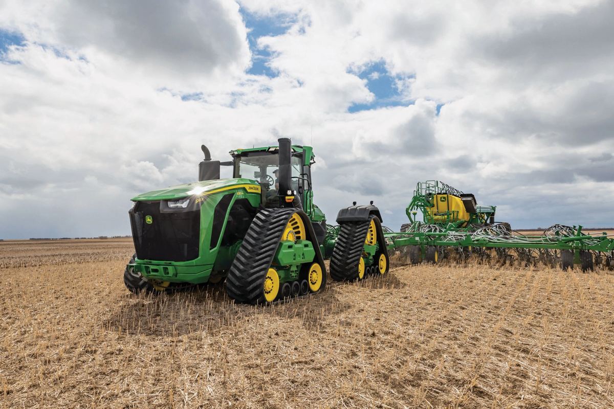 A John Deere tracked tractor with a StarFire receiver on its roof pulls an implement through a field under a cloudy sky