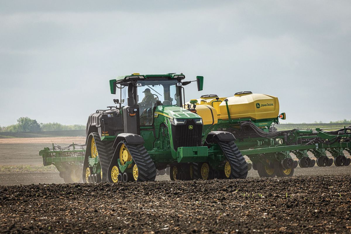 A John Deere 8R series tracked tractor pulling a large yellow planter across a field