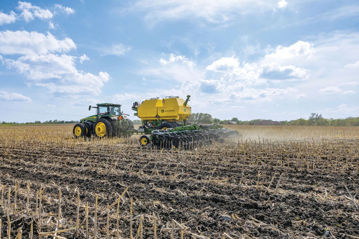 John Deere tractor pulling a yellow air cart and green tillage implement in a field