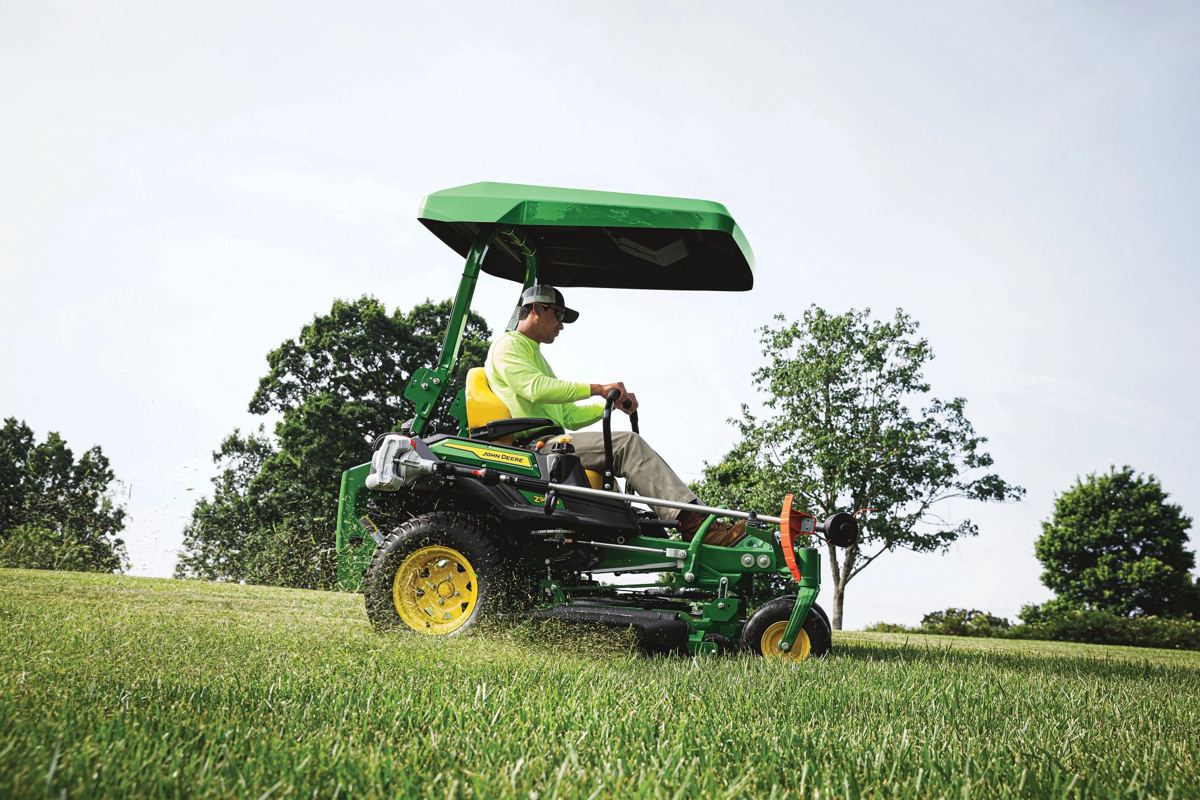 Man operating a John Deere Z994R zero-turn mower with a canopy on a grassy hill, cutting grass