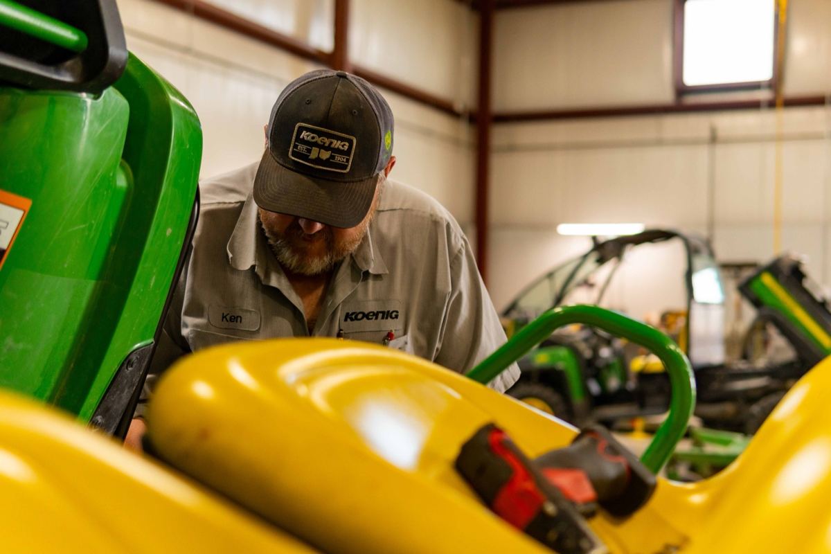Koenig Equipment technician Ken works on a green John Deere machine in a workshop