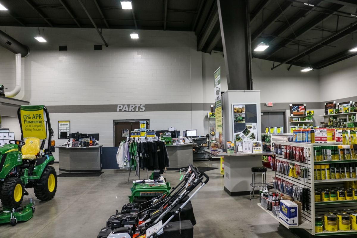 John Deere dealership interior showing a 2025R compact utility tractor, lawnmowers, parts counter, and product shelves