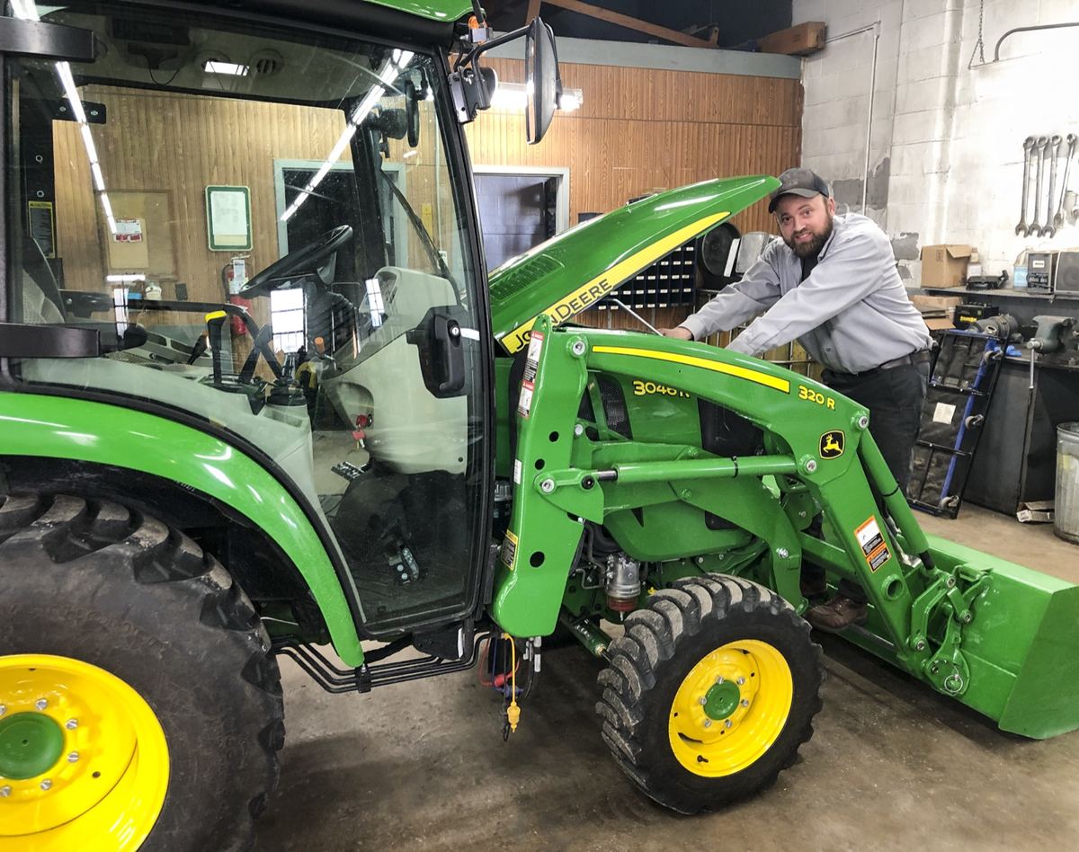Man standing next to a green John Deere 3040R tractor with an open hood and 320R loader