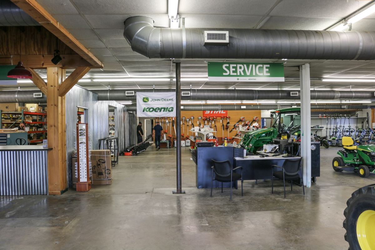 John Deere Koenig Equipment dealership interior with green tractors, Stihl power tools, a service desk, and two men
