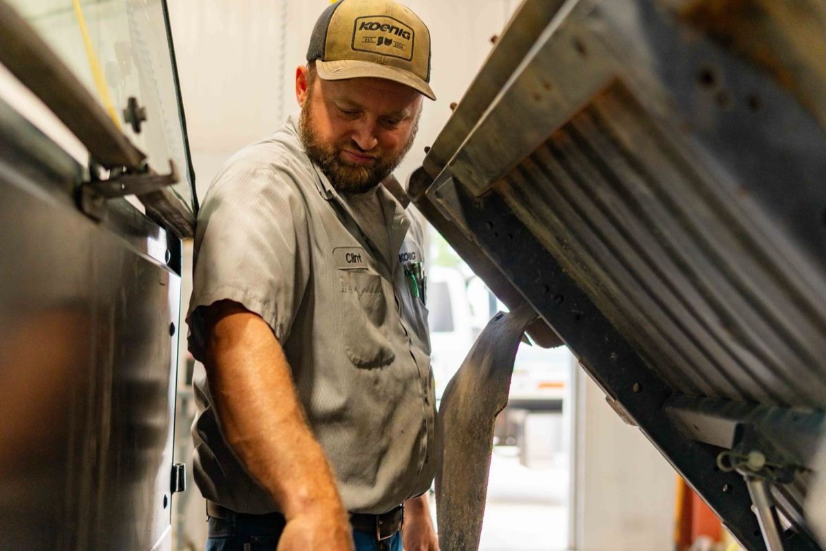 Technician wearing a Koenig John Deere cap and work shirt inspecting equipment