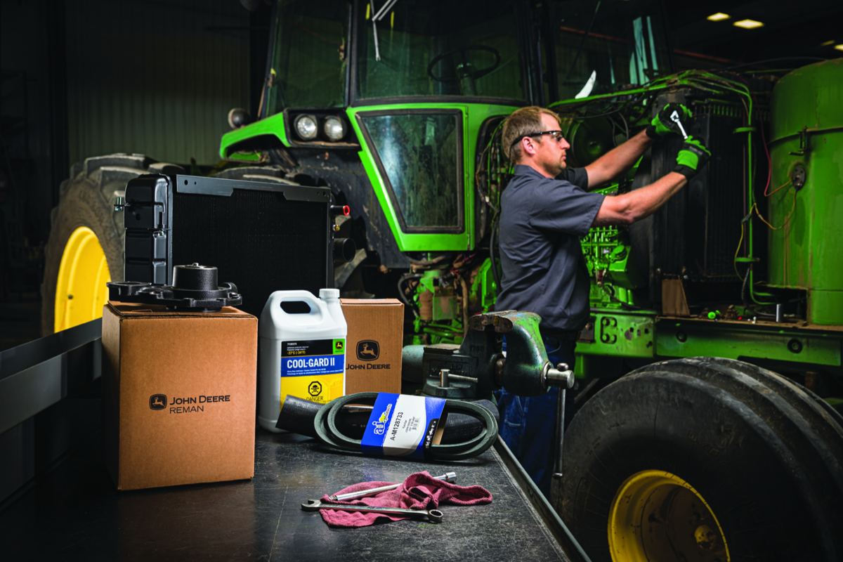 Mechanic repairing a John Deere tractor with John Deere REMAN parts, COOL-GARD II coolant, and a new belt