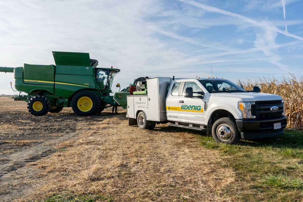 Green John Deere S780 combine and white Koenig Equipment service truck in a farm field