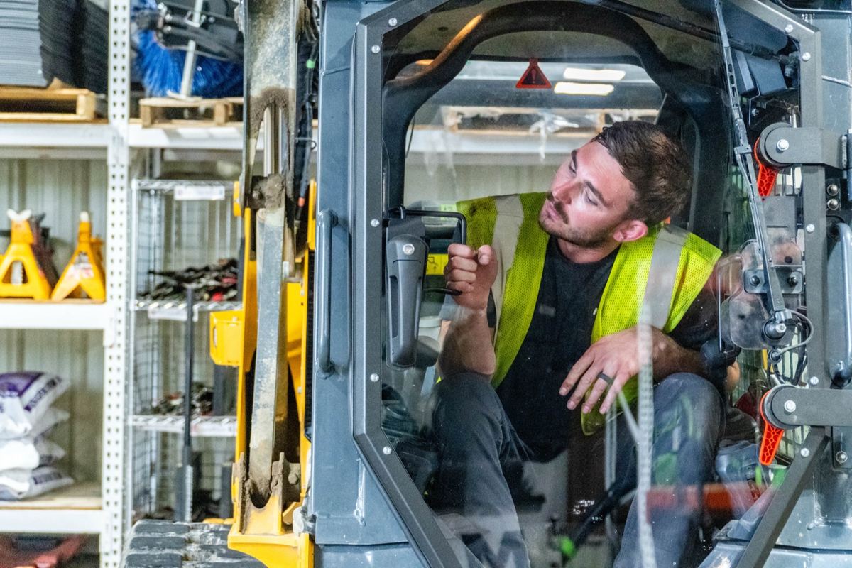 Man in a yellow safety vest operating a compact track loader inside a storage facility