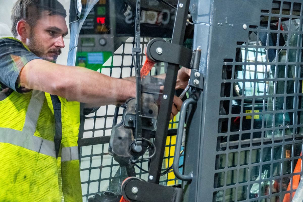 Man in yellow vest working on controls inside a gray heavy machinery cab