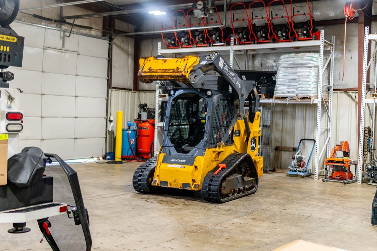 John Deere 317G compact track loader with a bucket in a warehouse with shelves of equipment
