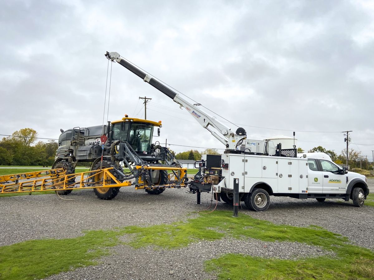 Koenig John Deere service truck with a Stellar crane assisting a Hagie agricultural sprayer on a gravel lot