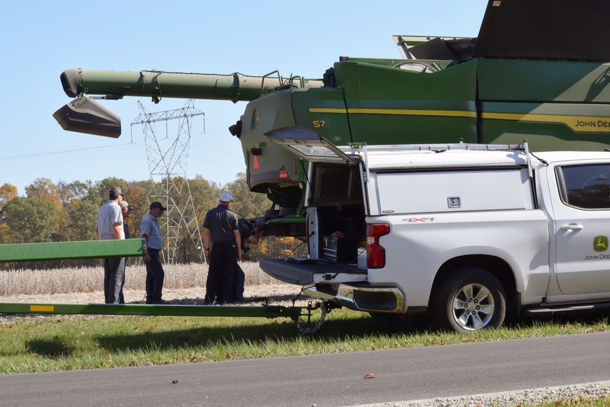 John Deere S7 combine and white John Deere service truck with technicians in a field