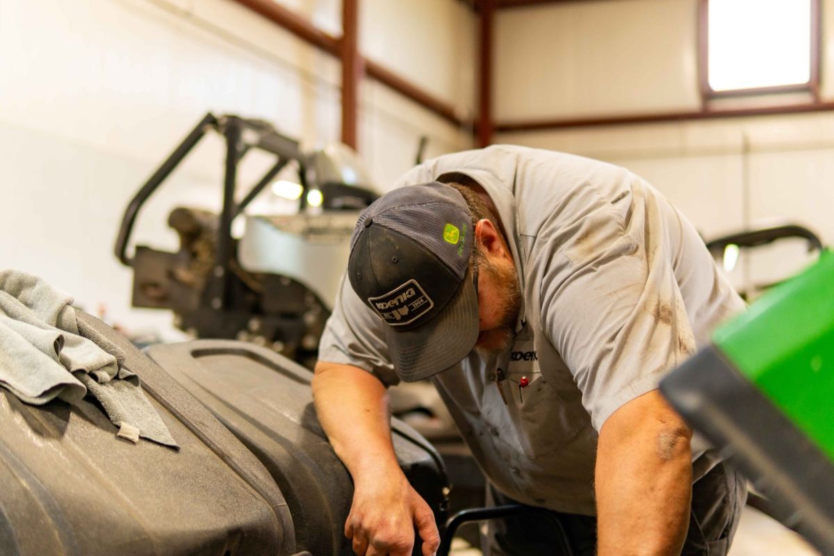 Man wearing a Koenig Equipment hat and shirt working on equipment in a service bay