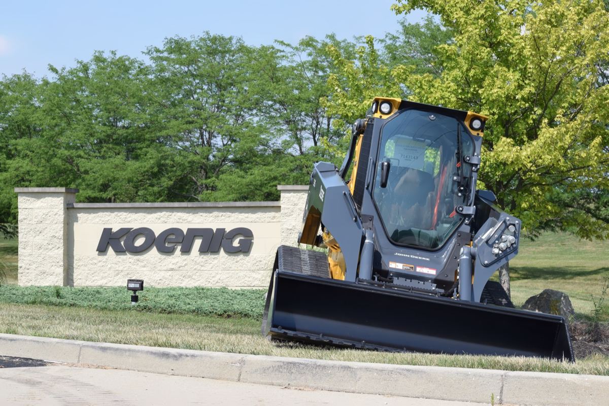 A John Deere compact track loader parked on the grass in front of a Koenig Equipment dealership sign