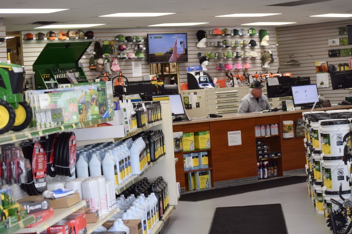 Interior of a John Deere dealership with shelves of parts, oils, tools, apparel, and a man at the service counter
