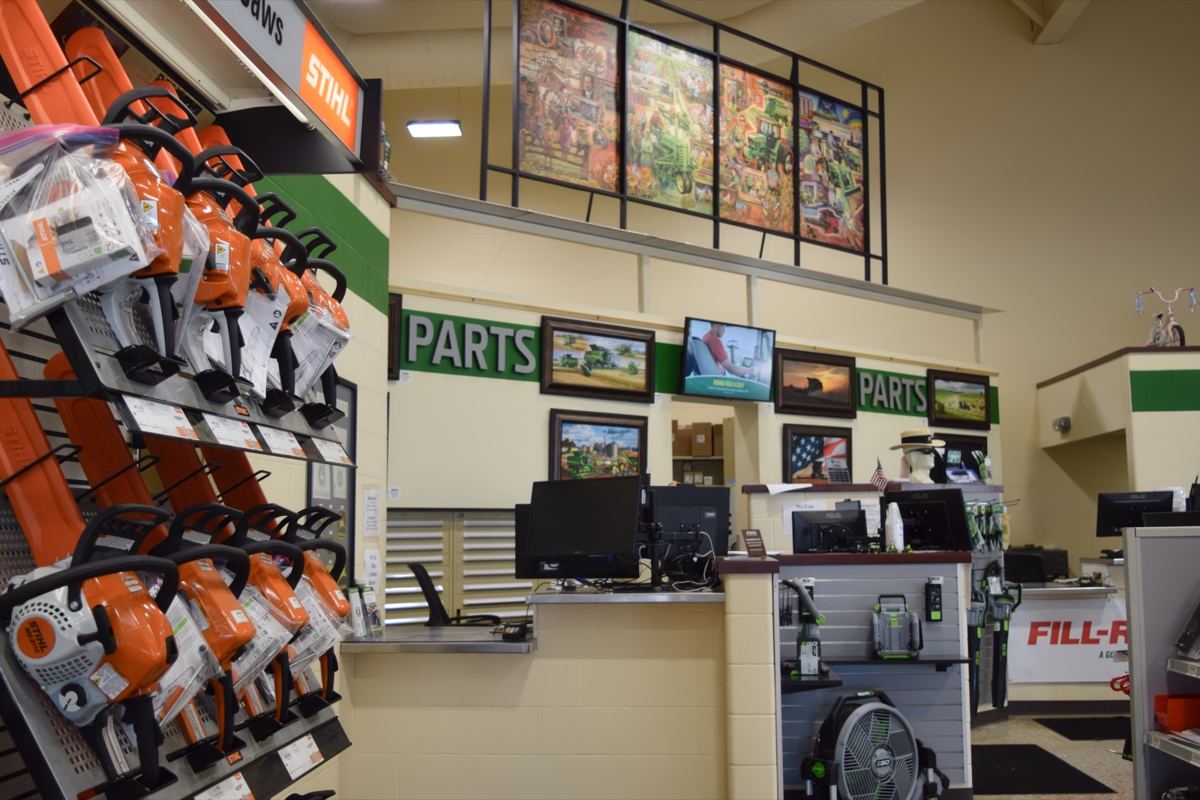 Stihl chainsaws on display near a parts counter with monitors and John Deere themed art