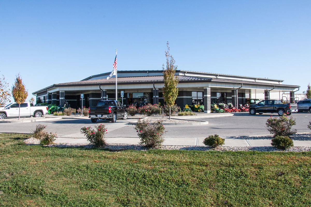 Exterior view of a dealership building with John Deere equipment and pickup trucks parked outside under a clear sky