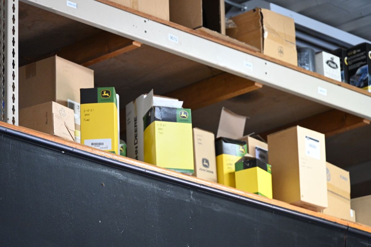 Warehouse shelves stocked with various cardboard boxes, including many John Deere parts boxes