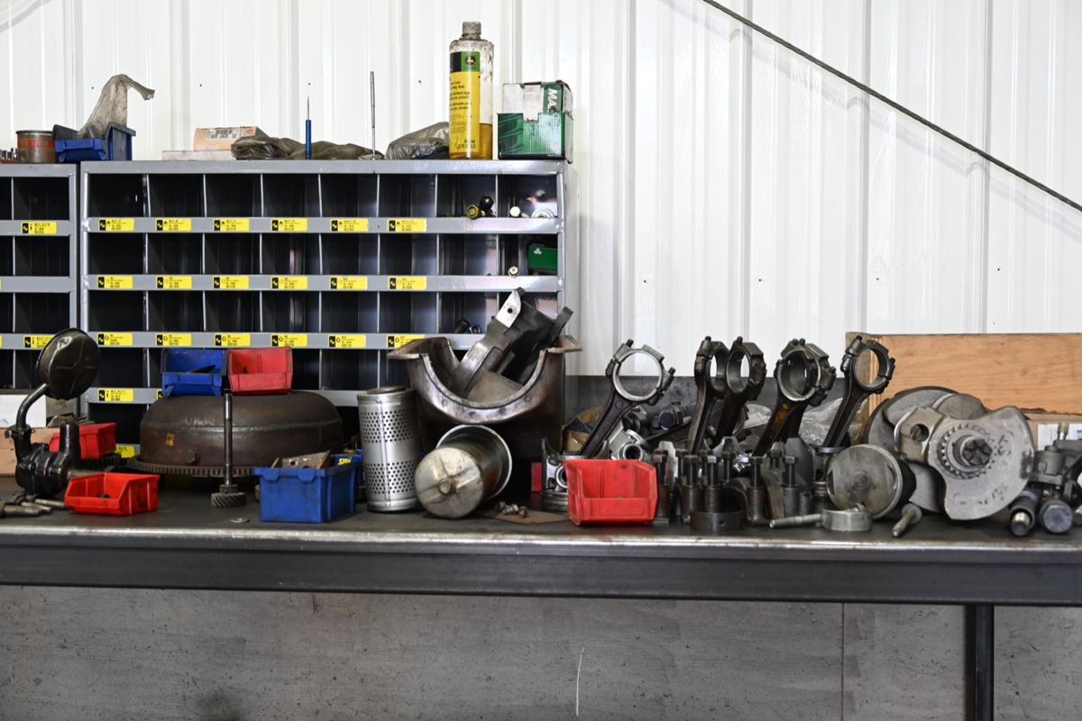 Workbench with various engine parts, filters, plastic bins, and a John Deere oil bottle on a shelf