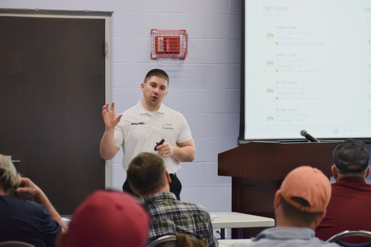 Koenig Equipment presenter speaks to an audience with a screen displaying 'High Alerts' and tractor icons