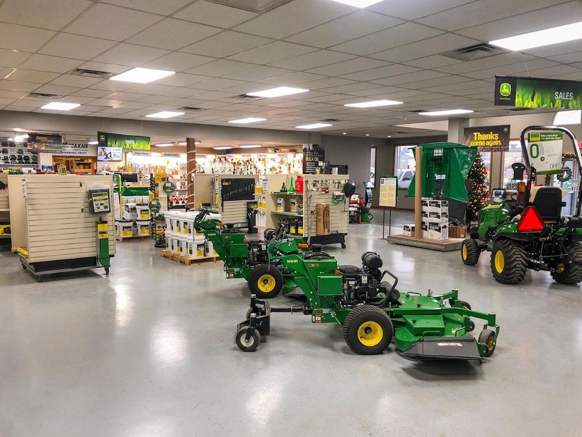 John Deere dealership showroom with green lawn care equipment, a tractor, and parts on shelves
