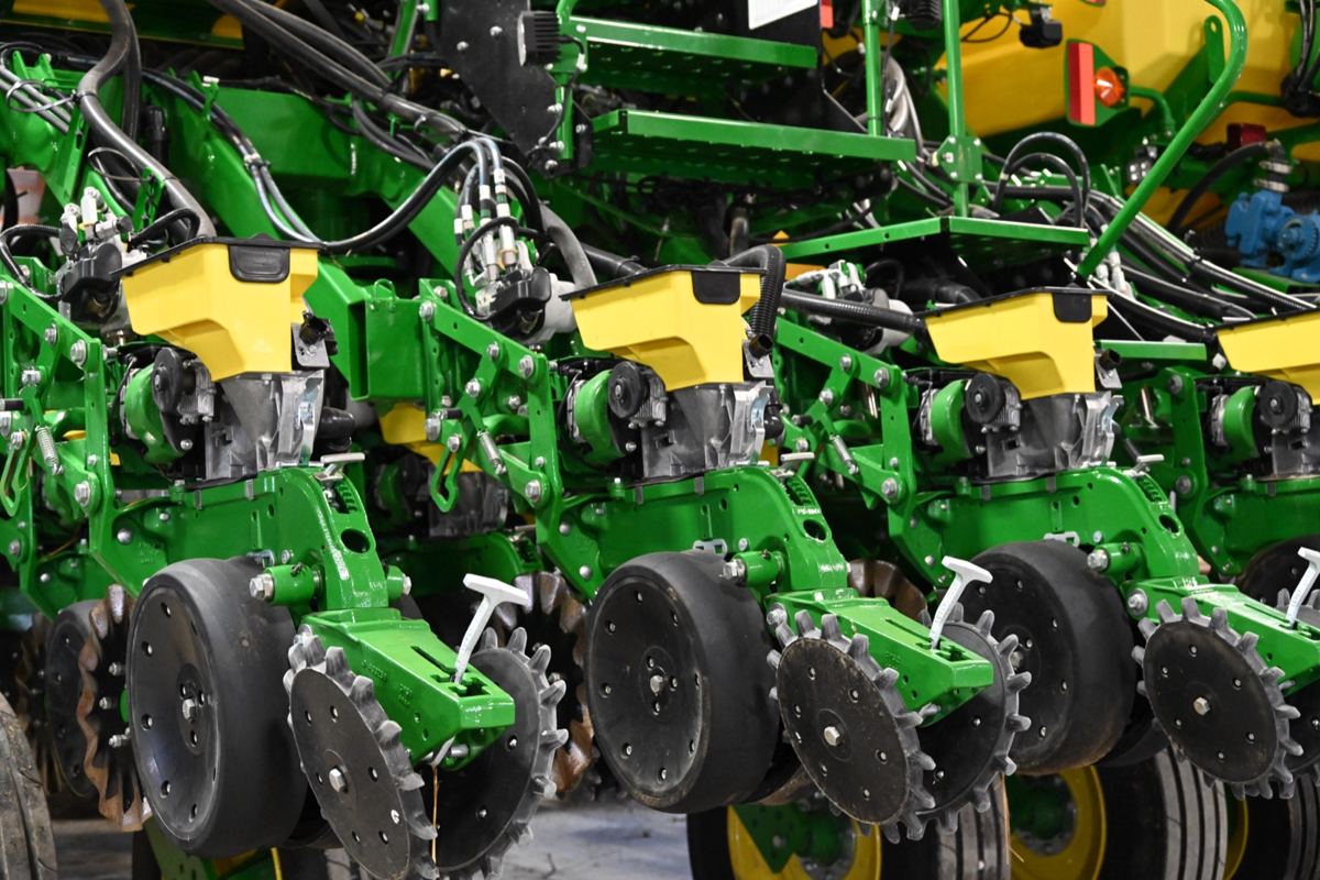 Close-up of multiple green and yellow John Deere planter row units with hoppers, wheels, and mechanical components