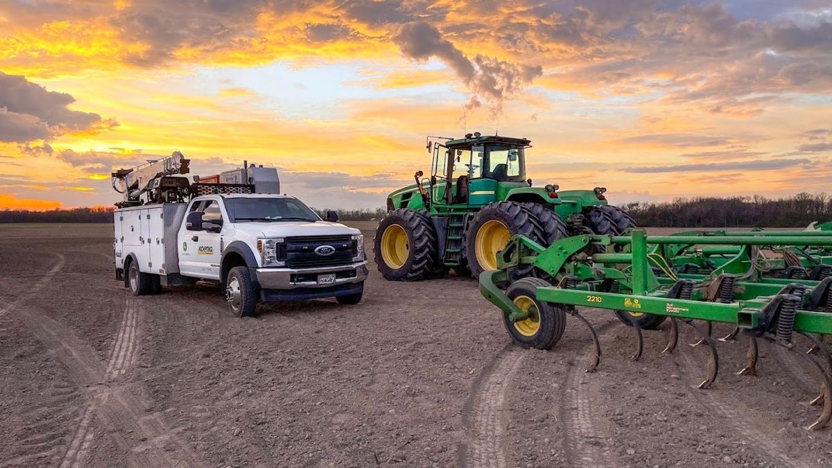 White Koenig service truck and green John Deere tractor with a 2210 field cultivator in a farm field at sunset
