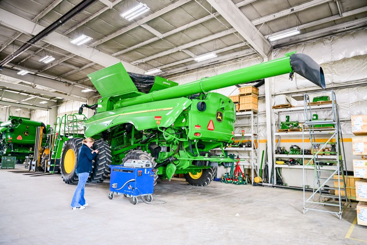 Woman standing next to a large green John Deere combine in a service bay with equipment