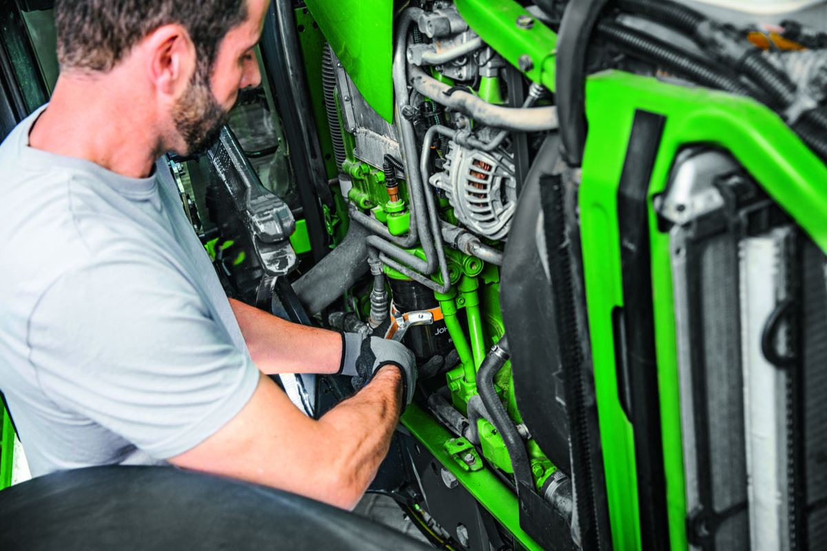 Man in gloves using a wrench to service the green engine of a John Deere tractor