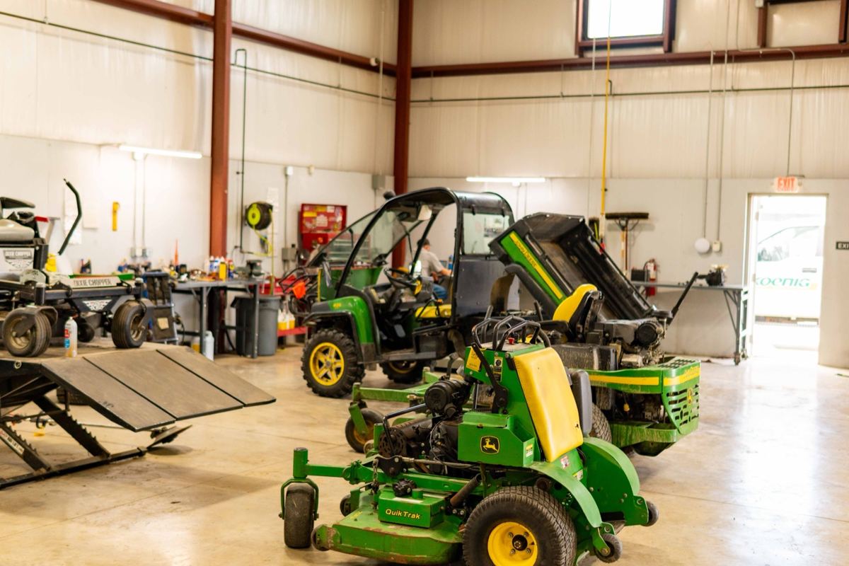 John Deere QuikTrak stand-on mower, Gator, and other equipment in a Koenig Equipment service bay
