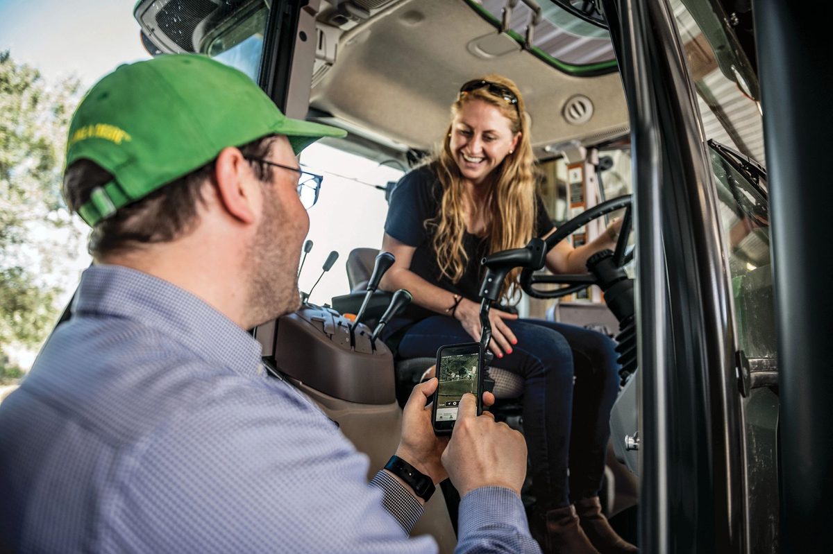 Man showing John Deere Operations Center on his phone to an operator sitting in a tractor cab